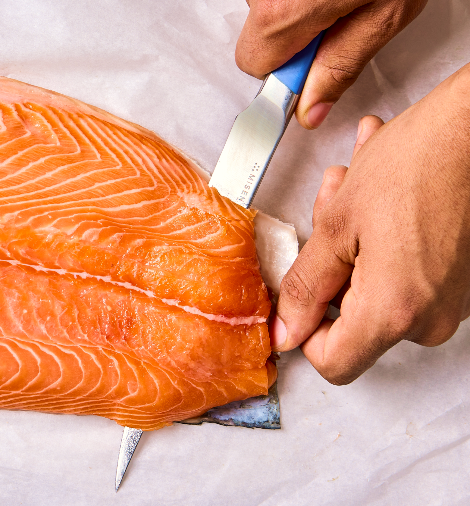 Removing skin from fresh salmon fillet with Misen knife on parchment paper