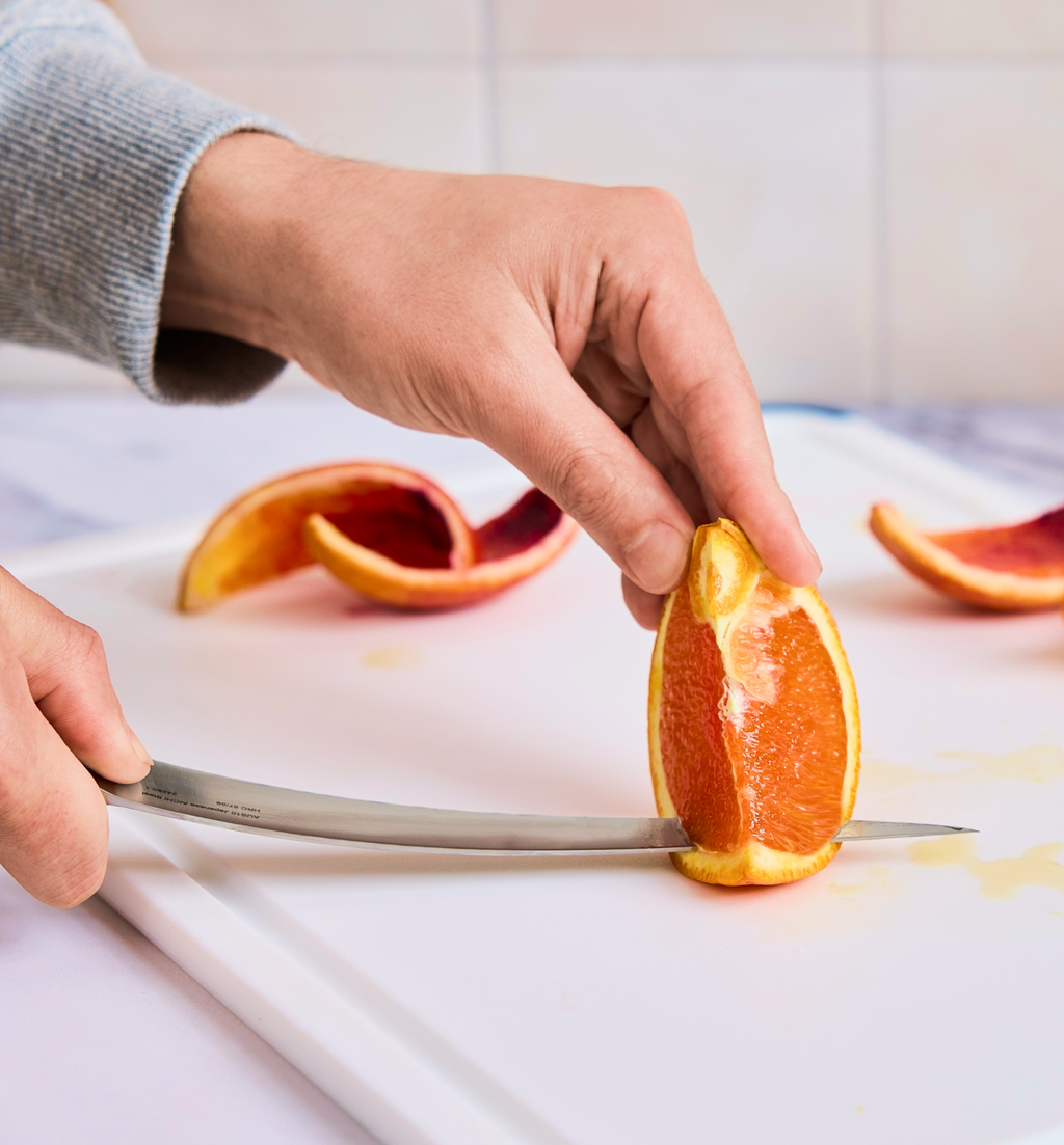 Hands slicing a blood orange on white cutting board with knife